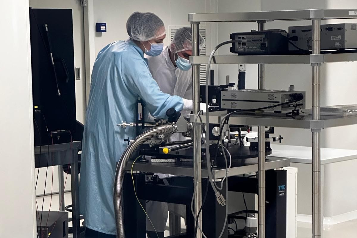 Two people in cleanroom gowns working together at the probe station.